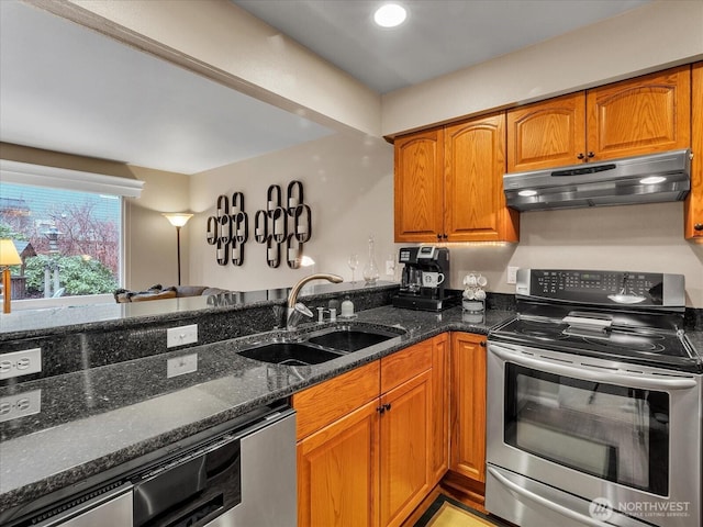 kitchen with dark stone counters, brown cabinets, stainless steel appliances, under cabinet range hood, and a sink