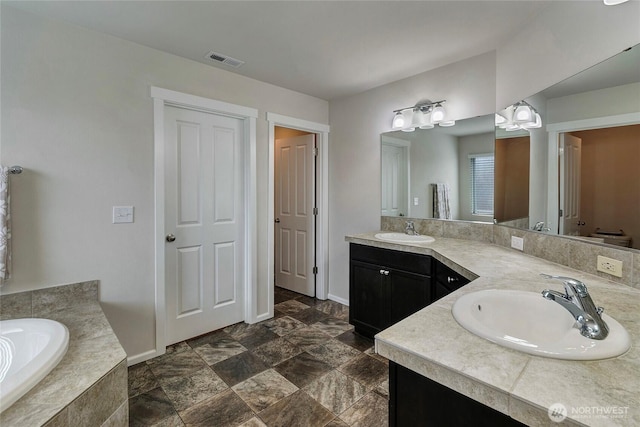 full bath featuring visible vents, a sink, a garden tub, and double vanity