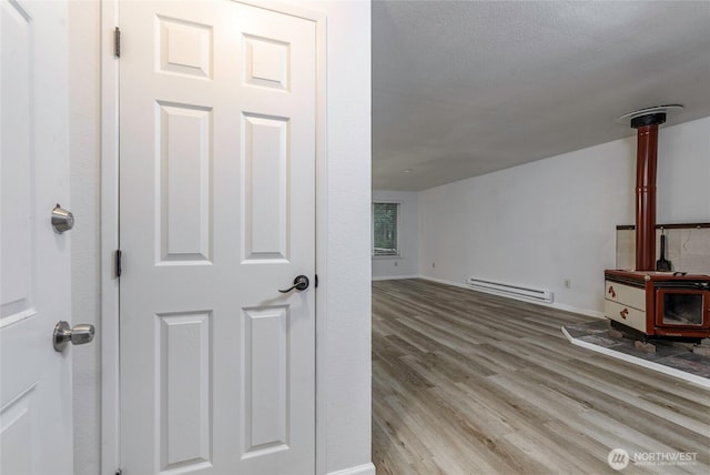 bonus room featuring a baseboard radiator, a wood stove, baseboards, and wood finished floors