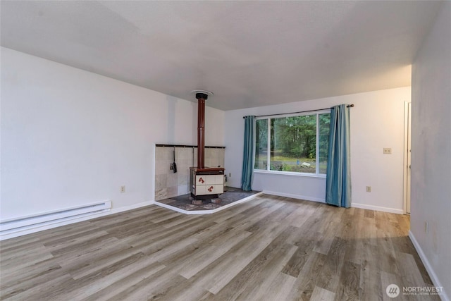 unfurnished living room featuring a baseboard heating unit, wood finished floors, a wood stove, and baseboards