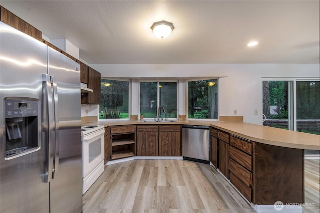 kitchen featuring stainless steel appliances, light countertops, a sink, a peninsula, and under cabinet range hood