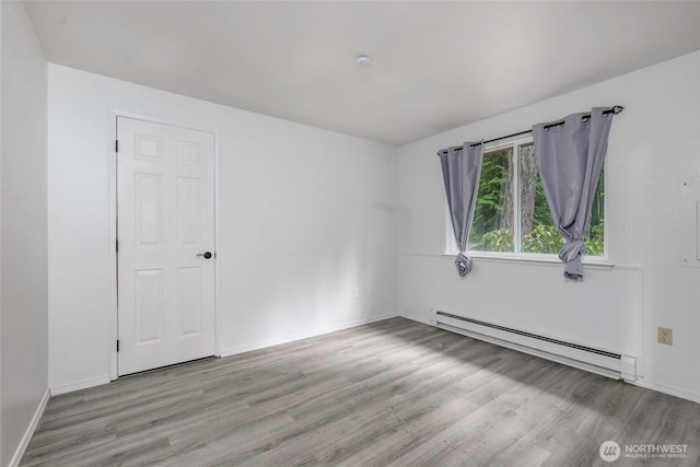 empty room with baseboards, a baseboard heating unit, and wood finished floors