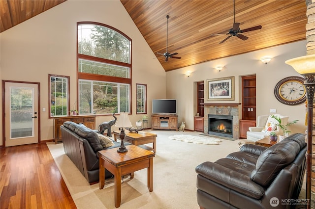 living area with high vaulted ceiling, wooden ceiling, a tile fireplace, baseboards, and light wood-style floors