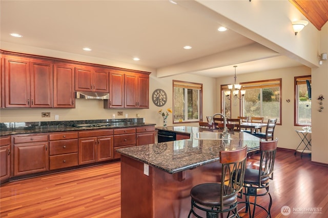 kitchen featuring black dishwasher, gas stovetop, a sink, under cabinet range hood, and a kitchen breakfast bar