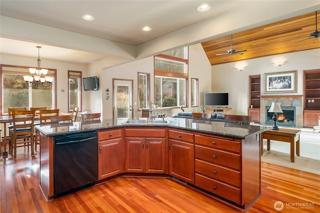 kitchen with dark stone counters, a fireplace, a sink, open floor plan, and dishwasher