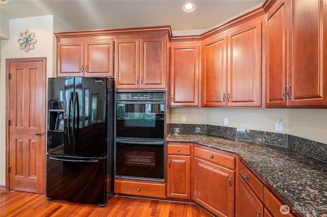 kitchen featuring brown cabinets, black appliances, dark stone counters, and wood finished floors