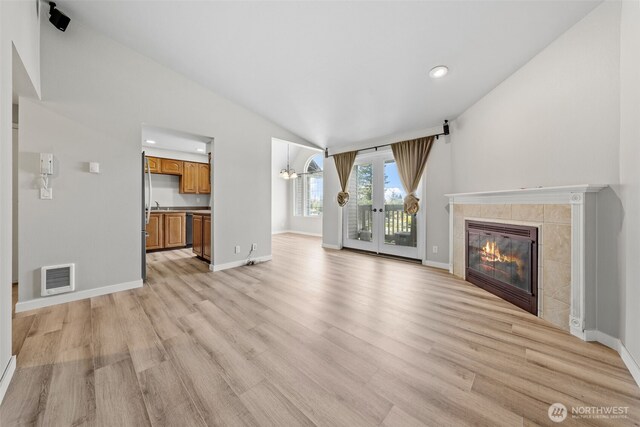 unfurnished living room featuring visible vents, lofted ceiling, a fireplace, baseboards, and light wood-type flooring