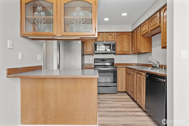 kitchen featuring glass insert cabinets, appliances with stainless steel finishes, a sink, a peninsula, and light wood-style floors