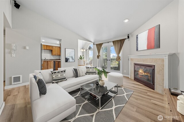 living room featuring light wood-style floors, baseboards, lofted ceiling, and visible vents