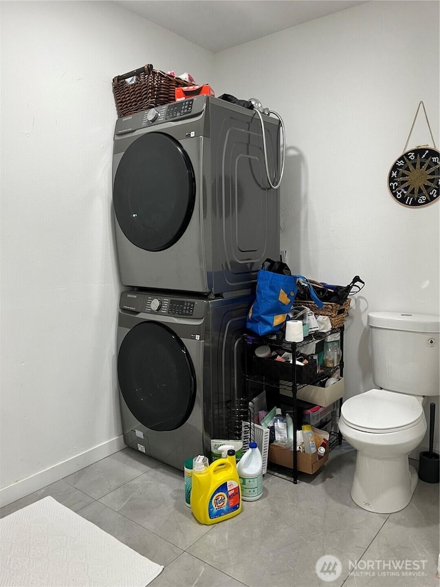 washroom with laundry area, stacked washing maching and dryer, tile patterned flooring, and baseboards