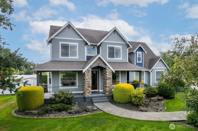 craftsman-style house featuring stone siding, covered porch, a shingled roof, and a front lawn