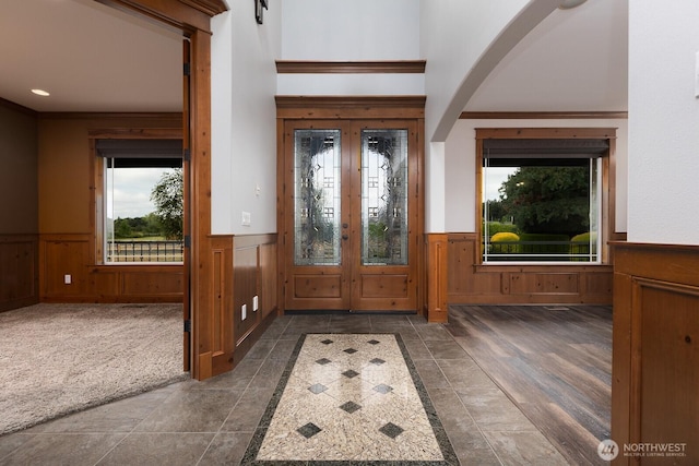 foyer with arched walkways, dark colored carpet, french doors, and wainscoting