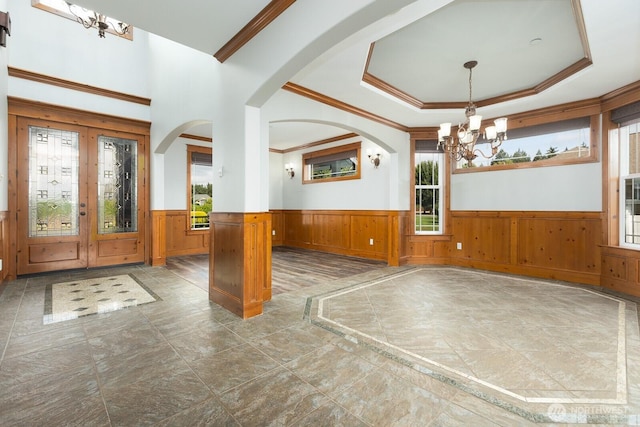 entryway with arched walkways, a chandelier, wainscoting, a tray ceiling, and crown molding