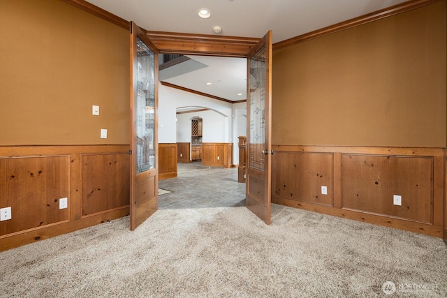 spare room with arched walkways, a wainscoted wall, recessed lighting, ornamental molding, and carpet flooring