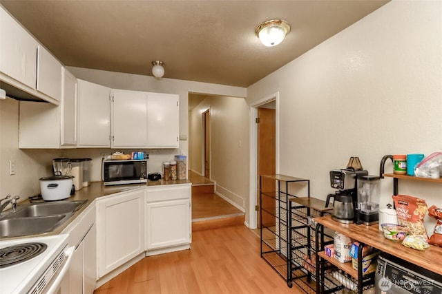 kitchen with white electric range oven, light wood-style floors, white cabinets, a sink, and black microwave