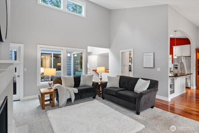 living room with light wood-style floors, a high ceiling, baseboards, and light colored carpet