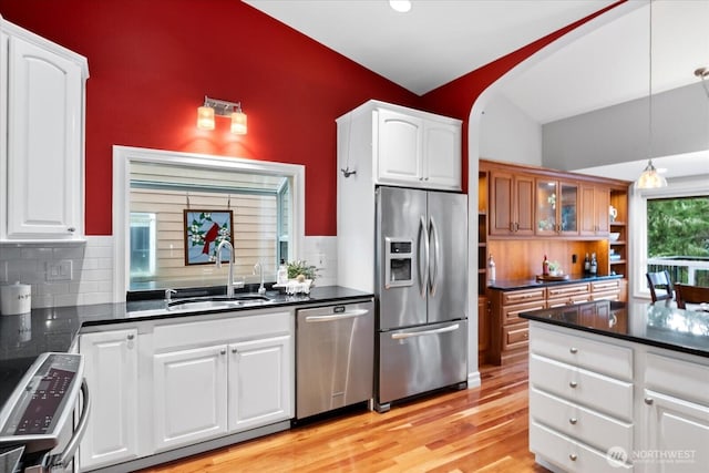 kitchen with white cabinets, dark countertops, light wood-style flooring, appliances with stainless steel finishes, and a sink