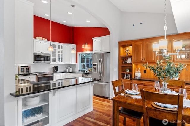 kitchen featuring dark countertops, appliances with stainless steel finishes, glass insert cabinets, a sink, and high vaulted ceiling