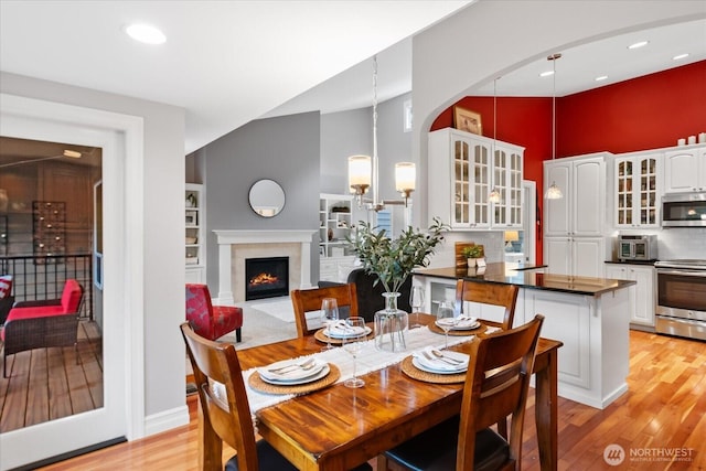 dining room featuring a lit fireplace, a high ceiling, light wood-type flooring, and a notable chandelier