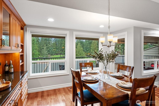 dining room featuring light wood-type flooring, a healthy amount of sunlight, baseboards, and an inviting chandelier