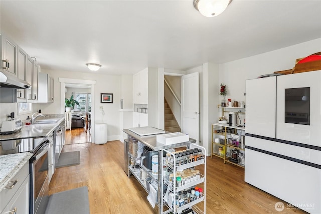 kitchen featuring light wood-style flooring, a sink, stainless steel range with electric cooktop, light countertops, and baseboards