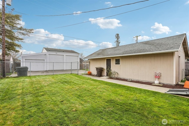 rear view of house with an outbuilding, fence, a shingled roof, a detached garage, and a lawn