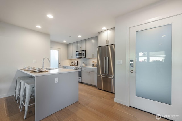 kitchen featuring tasteful backsplash, appliances with stainless steel finishes, a breakfast bar, gray cabinetry, and light wood-style floors