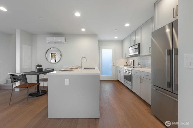 kitchen featuring a wall mounted AC, appliances with stainless steel finishes, a sink, and wood finished floors