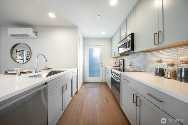 kitchen with stainless steel appliances, gray cabinetry, light wood-style floors, a sink, and a wall mounted AC