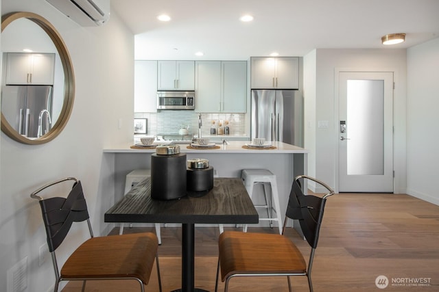 kitchen with a peninsula, light wood-style floors, light countertops, appliances with stainless steel finishes, and decorative backsplash