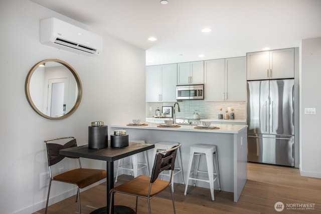 kitchen featuring a wall unit AC, light countertops, backsplash, appliances with stainless steel finishes, and light wood-style floors