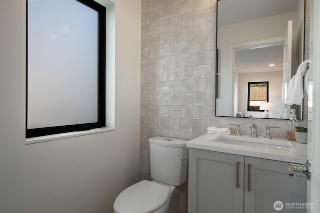 bathroom with toilet, tile walls, and vanity