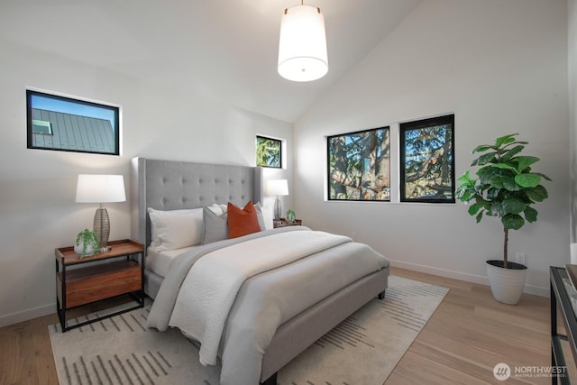 bedroom with lofted ceiling, light wood-style flooring, and baseboards