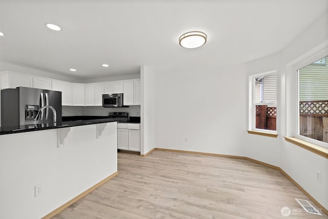 kitchen featuring visible vents, a kitchen bar, light wood-type flooring, white cabinets, and stainless steel appliances