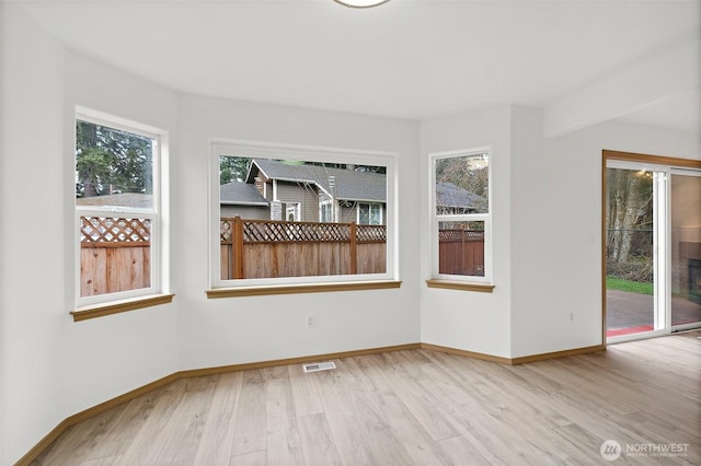 spare room with plenty of natural light, wood finished floors, visible vents, and baseboards