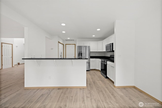 kitchen featuring dark countertops, white cabinets, stainless steel appliances, and light wood-style floors