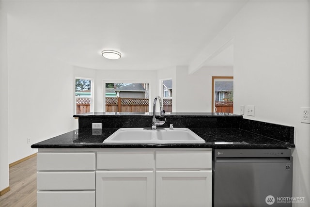 kitchen featuring light wood finished floors, dishwasher, dark stone countertops, white cabinetry, and a sink