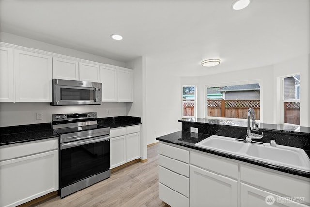 kitchen with appliances with stainless steel finishes, white cabinetry, light wood-type flooring, and a sink