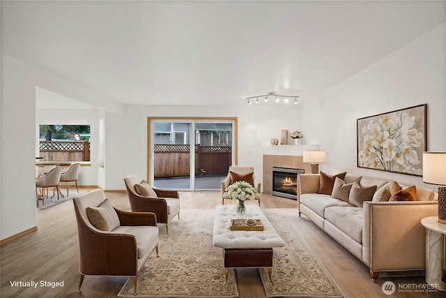 living room with light wood finished floors, a tile fireplace, and baseboards