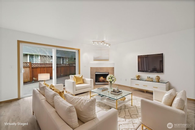 living area with baseboards, light wood-type flooring, and a tile fireplace