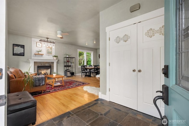 foyer entrance featuring a lit fireplace, dark wood-type flooring, and a ceiling fan