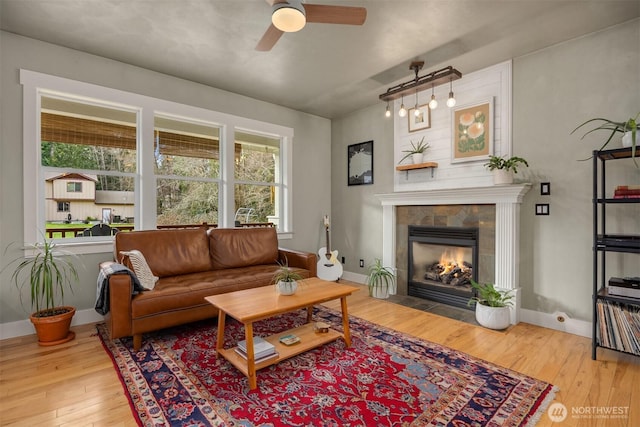 living area featuring ceiling fan, hardwood / wood-style floors, a fireplace, and baseboards