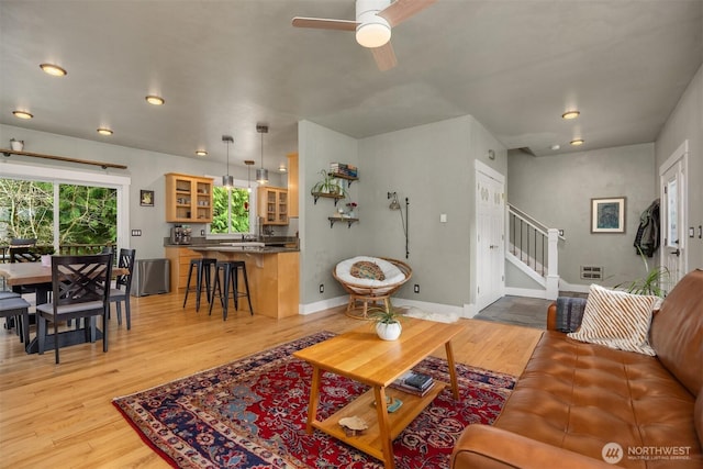 living room with light wood finished floors, ceiling fan, stairway, and baseboards