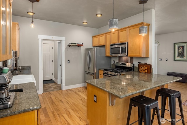 kitchen featuring stainless steel appliances, a peninsula, a sink, light wood-style floors, and a kitchen bar