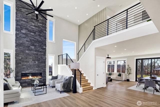 living room with baseboards, ceiling fan, stairway, a stone fireplace, and light wood-type flooring