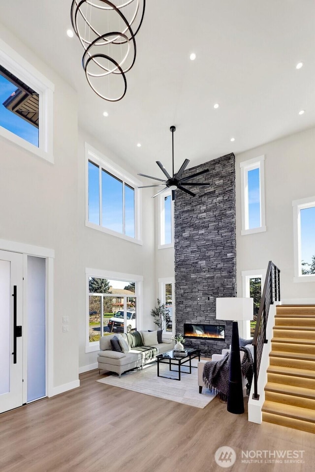 living room featuring stairway, wood finished floors, ceiling fan with notable chandelier, a fireplace, and recessed lighting