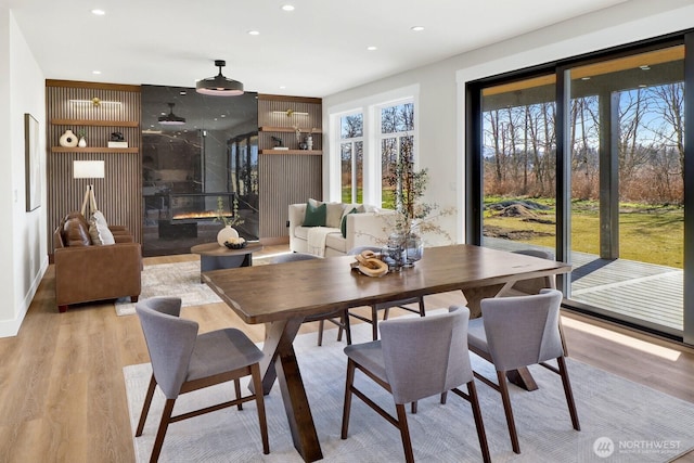 dining area with a premium fireplace, light wood-style flooring, and recessed lighting