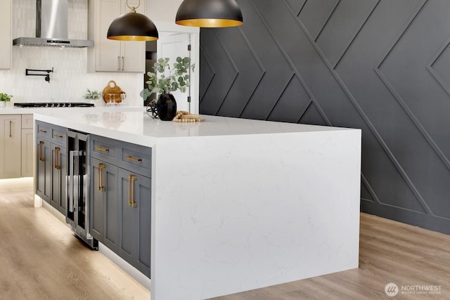 kitchen with wine cooler, light countertops, light wood-type flooring, stovetop, and wall chimney exhaust hood