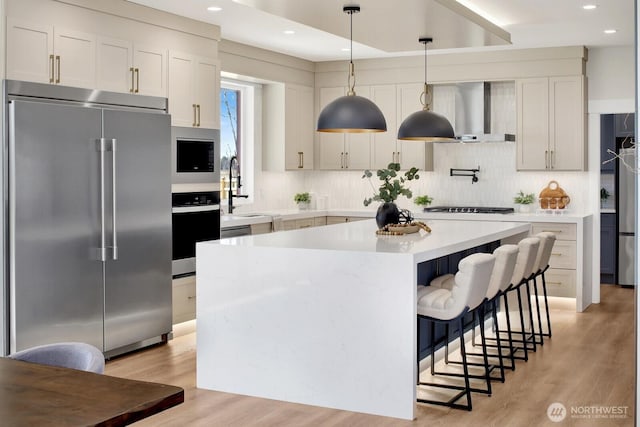 kitchen featuring built in appliances, a kitchen island, a sink, light countertops, and light wood-type flooring