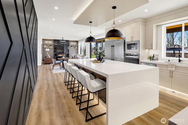 kitchen with a breakfast bar area, stainless steel appliances, a spacious island, a sink, and light wood-type flooring